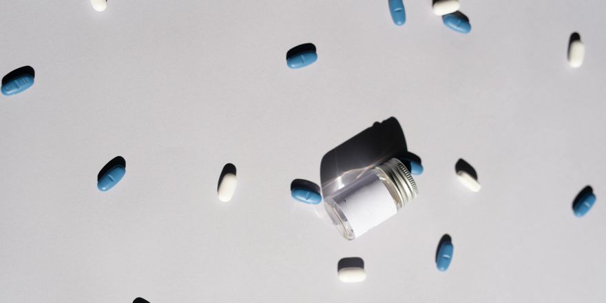 compresse bianche e blu sparse su superficie bianca con boccetta di vetro vuota rovesciata